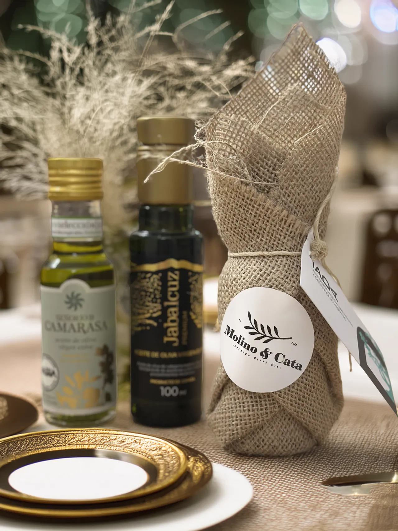 detalle de boda: botella de aceite Molino y Cata envuelta en arpillera sobre la mesa del banquete